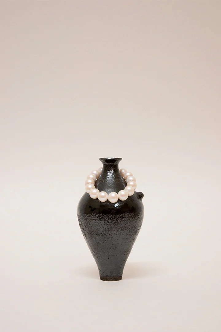 Artisanal handmade wheel-thrown ceramic vase tableware set. Dark Glaze ceramics. Hand built vessel with white pearl and silver bracelet.